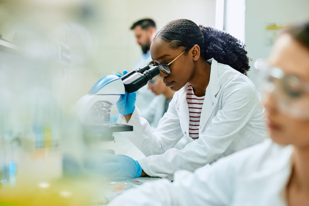 Female scientist examining a tissue slide using immunohistochemistry (IHC) under a microscope in a laboratory setting.
